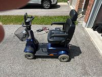 Side view of left side of blue mobility scooter on driveway, showing basket, foot platform and seat