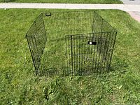 Full view of the black metal wire pet cage on grass, showing its rectangular shape and open inside.
