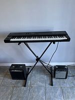 Roland D-10 keyboard on black X-style keyboard stand with two amps on floor, cables visible