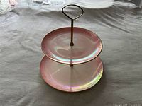 Full view of the two-tier serving plate showing iridescent pink tiers with gold trim, metal central rod with loop handle