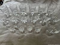 Seventeen-piece set displaying various sizes of faceted crystal glasses and bowls, arranged in rows on fabric surface.