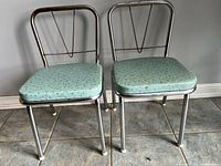 Two mid-century modern style children's chairs seen from the front, showing light turquoise patterned vinyl seats on chrome tubular metal frames.