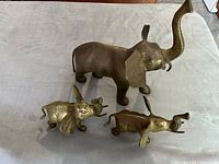 Photo of three brass elephant figurines, large one in the back with raised trunk and missing tusk, two smaller elephants in front