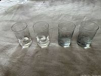Four clear drinking glasses with etched floral patterns shown in natural light on a textured surface.