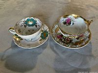 Front angle of both Shafford bone china cups on three legs with matching saucers showing florals and gold accents