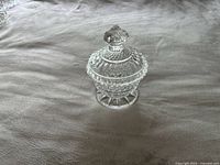 Photo of a small crystal glass bowl with a diamond pattern and pedestal base, shown with lid on top featuring a faceted knob.