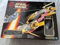 Front of the box showing Star Wars Episode I branding, image of podracer with yellow engines and included Anakin Skywalker figure visible through window.