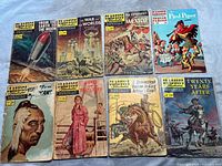 Photo showing 10 Classics Illustrated Junior comic books laid out in two rows with various titles including From the Earth to the Moon, War of the Worlds, The Conquest of Mexico, The Pied Piper, and others with visible wear and damage on covers