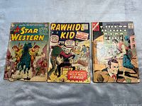 Front covers of three vintage Western comics: All Star Western, Rawhide Kid, Wyatt Earp on a neutral fabric background