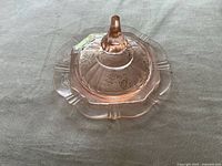 Overhead photo showing the pink glass serving dish with the matching conical lid, highlighting the floral etched design and the shape of the dish with scalloped rim.