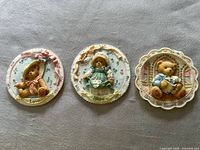 Front view of three multicolored resin Cherished Teddies wall plaques, each with a unique teddy bear design and decorative border.