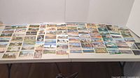 Wide view of the table fully covered with arranged postcards, showing many scenic representations across the collection.