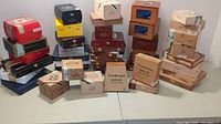 Overview of 43 assorted wooden cigar boxes in multiple sizes and colors, stacked and grouped by color on table.