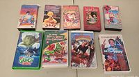 Photo showing 9 Christmas-themed VHS tapes arranged in two rows, titles include Frosty the Snowman, Grinch, Jingle All The Way, Santa Claus and others.