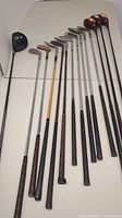 Full view of 13 golf clubs with wooden and steel shafts, including woods and irons.