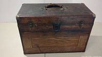 Front view of the wooden machinist chest showing three metal clasps and a leather handle.