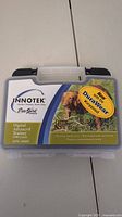 Plastic carrying case labeled INNOTEK Digital Advanced Trainer ADV-1000P with photo and branding sticker.