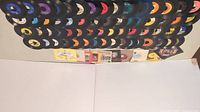 Wide view showing a large collection of over 100 assorted 45 rpm vinyl records with assorted label colors and designs, some in paper sleeves.