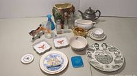 Full view of assorted glassware, china, pottery, collectible bottles, and decorative items arranged on white surface, showing all included items in the lot.