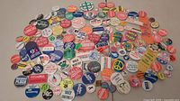Photo of a large group of political and nametag pins showing varied messaging, designs, and colors spread on a flat surface.