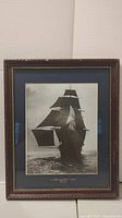 Full view of the framed black and white art print showing the ship "Monongahela" sailing with full sails, framed under glass in a worn wooden frame.