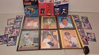 Display of six framed baseball puzzle posters with players Stan Musial, Willie Stargell, Rod Carew, Harmon Killebrew, Carl Yastrzemski, Warren Spahn plus three Starting Lineup figures and assorted baseball cards on table.