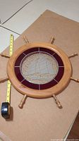 Full view of the stained glass ship's wheel wall hanging with measuring tape showing roughly 20 inch width.