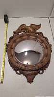 Full view of the vintage curved wall mirror with eagle detail and tape measure for scale.
