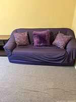Front view of purple slipcovered loveseat with three pillows