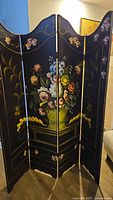 Front view of the black wooden room divider showing the hand-painted floral artwork on all panels.