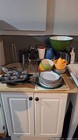 Full view of kitchen items on countertop including bowls, mugs, plates, glasses, muffin tin, and toast rack