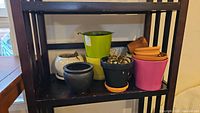 Photo of various plant pots on shelving including white ceramic pot, black pots, and colorful plastic pots