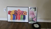 Two floral prints and one wall clock arranged on floor against wall.