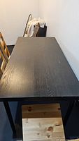 Top view of rectangular black wooden dining table with visible wood grain and minor surface scratches.
