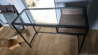 Side angled view of metal table with clear glass top and wooden shelf below, showing overall dimensions and condition.