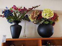 Two ceramic vases with artificial flowers and clear bud vase on shelf