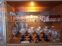 Shelf of assorted stemware showing blue-stem coupes, wine goblets and frosted snifters