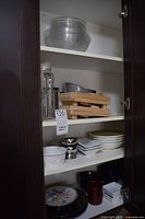 Cabinet view showing stacked glass plates, glass bottles, wooden cutting boards, bowls and dishes