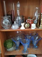 Upper shelf showing decanter, covered dish, hurricane chimneys, brass candlesticks, small ceramics and metal pieces
