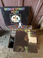 Photo showing Sesame Street Fever album and Dan Hill Longer Fuse album atop crate of records.