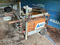 Side angle view of the arc welder showing rusted metal frame, coiled power cables, and Airco label.