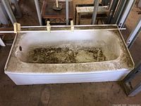 White metal bathtub viewed from the side showing heavy dirt inside and on edges, metal frame construction.