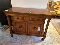 Front view of wood cabinet showing drawer and double doors with metal pulls and castor wheels