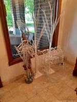 Christmas decor items grouped near a mirror, including two white artificial trees, wireframe reindeer light figure, and glass vase with branches.