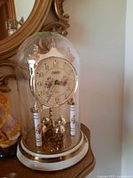 Photo of a decorative anniversary table clock with a floral dial under a clear glass dome with gold and cream base