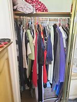 Closet rod with assorted ladies clothing including shirts, skirts, cardigans, hoodies hung on hangers.