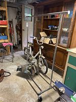 Full view of chrome adjustable metal clothing rack beside a bicycle in a basement workroom.