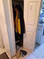 Black and yellow Nike winter jacket hanging on closet rod with several other clothing items, brown leather and black fabric work gloves on floor below.