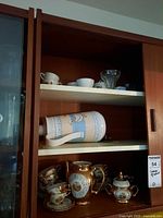 Shelf with Made in Japan coffee cups, glass ice cream cups on top and thermos lying horizontally on middle shelf above espresso coffee set on bottom shelf.