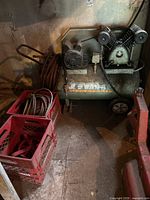 Full view of Swan air compressor in garage with attached hoses coiled on side, red milk crates visible nearby with extra hoses (not included).